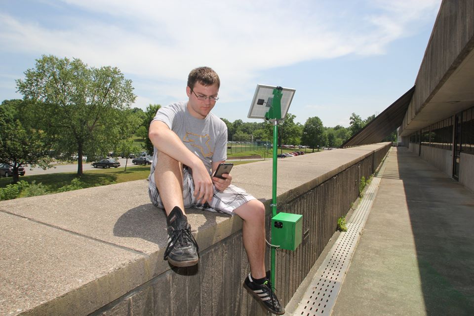 A male student charges his phone at a solar charging station